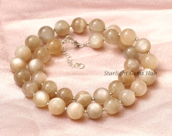 May include: A double strand necklace made with light brown moonstone beads. The necklace has a silver clasp and is approximately 18 inches long.  Starlight Gems Hub is printed on the fabric background.