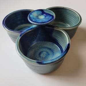 May include: A ceramic serving dish featuring three interconnected round bowls with a glossy glaze. The finish displays a gradient of deep cobalt blue at the rims and center points, transitioning into lighter shades of teal and seafoam green.