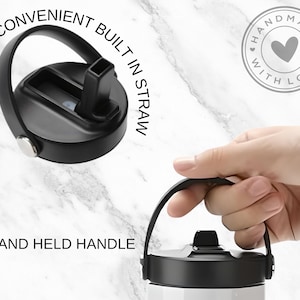 Op de afbeelding: Een zwarte roestvrijstalen waterfles met een ingebouwde rietje, een handvat en een deksel met een handige ingebouwde rietje. De fles staat op een wit marmeren oppervlak. De tekst "HAND HELD HANDLE" en "CONVENIENT BUILT IN STRAW" is zichtbaar op de afbeelding.
