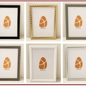 May include: Six picture frames with a decorative, raised, rope-like border. The frames are in black, gold, grey, silver, and white. Each frame has a white mount and a small orange image of an egg with the text "Dudley Dean" inside.
