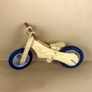 Puede incluir: Una bicicleta de equilibrio de madera con un manillar de madera marr&oacute;n y un acabado de madera natural. La bicicleta tiene neum&aacute;ticos de goma negra y un asiento de madera.