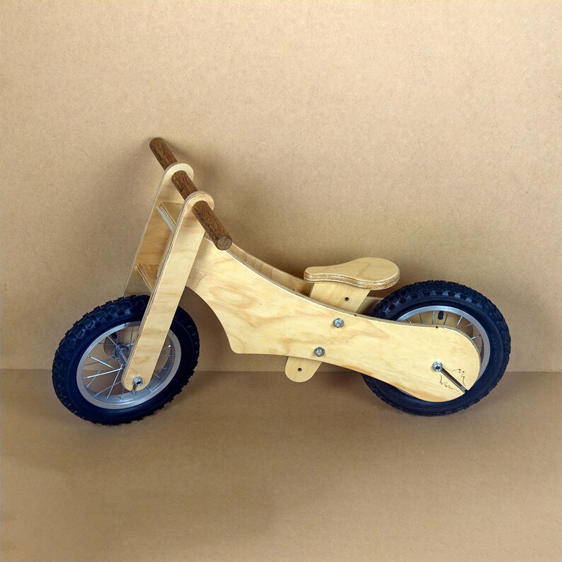 Puede incluir: Una bicicleta de equilibrio de madera con un manillar de madera marr&oacute;n y un acabado de madera natural. La bicicleta tiene neum&aacute;ticos de goma negra y un asiento de madera.