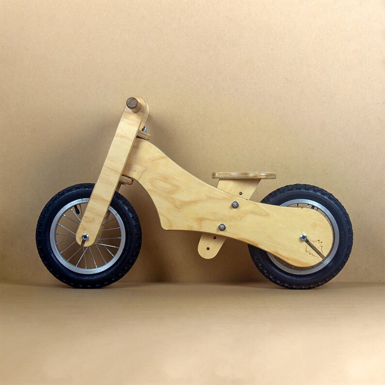 Puede incluir: Una bicicleta de equilibrio de madera con neum&aacute;ticos negros y un acabado de madera natural. La bicicleta tiene un dise&ntilde;o simple con un marco curvo y un asiento peque&ntilde;o.