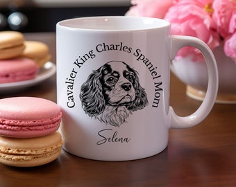May include: White ceramic coffee mug with a black and white illustration of a Cavalier King Charles Spaniel. The text "Cavalier King Charles Spaniel Mom" is written in a circle around the dog's head. The name "Selena" is written below the dog's head.