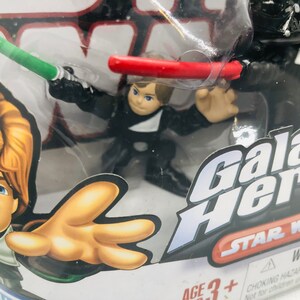 May include: A plastic package containing two Star Wars Galactic Heroes action figures. The figures are Luke Skywalker and Darth Vader. The package has a red, white, and black design with the words "Galactic Heroes" and "Star Wars" printed on it. The package also includes a warning label.