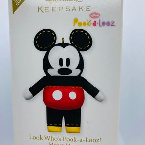 Puede incluir: Un adorno Hallmark Keepsake con Mickey Mouse en un diseño Pook-a-Looz rojo y negro. El adorno es una edición especial y está etiquetado como "Look Who's Pook-a-Looz! Mickey Mouse Special Edition".