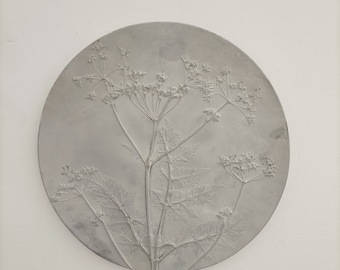 May include: A round, white ceramic plate with a raised, embossed design of a delicate flower with multiple stems and leaves.