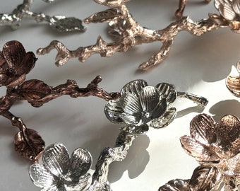 May include: A set of five silver and copper floral branch ring holders. The branches are detailed with textured leaves and flowers.