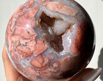 May include: A large, polished agate sphere with a natural geode opening revealing a white crystal interior. The sphere has a swirling pattern of pink, brown, and white.