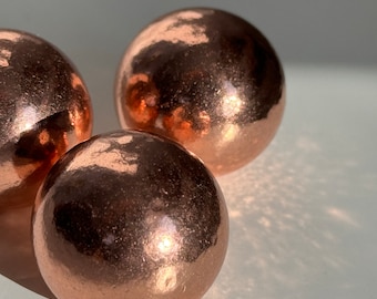 May include: Three shiny copper spheres, each with a smooth, reflective surface. The spheres are arranged in a triangular formation on a white background.
