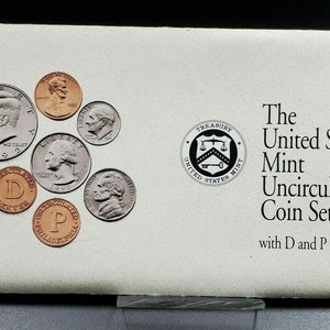 May include: A white cardboard coin set package with the text "The United States Mint Uncirculated Coin Set with D and P Mint Marks". The package contains a collection of silver and copper coins.