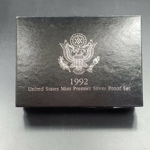 May include: A black box with a textured surface. The box features the United States Mint seal, the year "1992," and the text "United States Mint Premier Silver Proof Set" in silver lettering. The box is rectangular and sits on a dark surface.