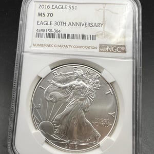 May include: A silver 2016 American Eagle coin, graded MS 70, encased in a protective holder. The coin features Lady Liberty and the text "IN GOD WE TRUST". The holder is labeled "EAGLE 30TH ANNIVERSARY" and includes the Numismatic Guaranty Corporation logo.