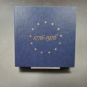 May include: A navy blue box with a gold circle of stars and the text "1776-1976" in gold.