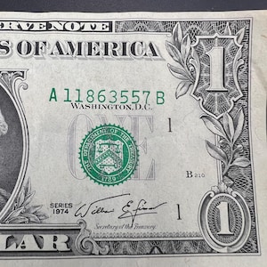 May include: A green one dollar bill with the serial number A 11863557 B. The bill is from the 1974 series and has the signature of William E. Simon, Secretary of the Treasury.