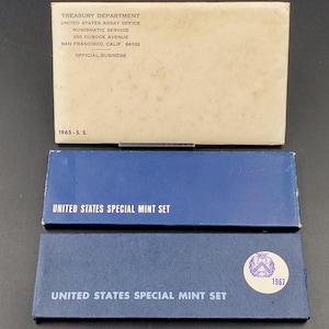 May include: A blue box with the text "United States Special Mint Set" and the year "1967" printed on it. The box is surrounded by a white envelope with the text "Treasury Department, United States Assay Office, Numismatic Service, 350 Duboce Avenue, San Francisco, Calif. 94102, Official Business" printed on it.