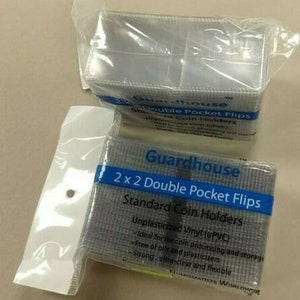 May include: Two packs of Guardhouse 2x2 Double Pocket Flips Standard Coin Holders. The packs are made of clear plastic and have a gray and white label with the text "Guardhouse 2x2 Double Pocket Flips Standard Coin Holders Unplasticized Vinyl (uPVC) Ideal for coin processing and storage Free of oils and plasticizers Strong, ultra-clear and flexible NUMISMATISTS WORLDWIDE".