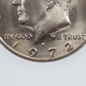 May include: Close-up of a silver US half dollar coin with the profile of John F. Kennedy on the obverse. The coin reads "In God We Trust" and "1972".