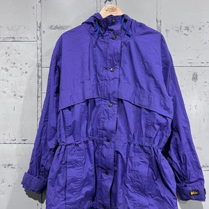 May include: A purple hooded jacket with a drawstring waist and a button closure. The jacket has a logo on the lower right side that says "K-Way".