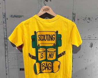 Camiseta gráfica de algodón y poliéster fino de los años 70 con diseño de mochila de las Girl Scouts en color amarillo mostaza, talla mediana
