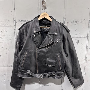 Könnte beinhalten: Schwarze Lederjacke mit Reißverschluss, mehreren Reißverschlusstaschen und einem Gürtel in der Taille. Die Jacke hat einen klassischen Biker-Stil mit Schulterklappen und einem Reverskragen. Die Jacke hängt an einem Holzbügel.