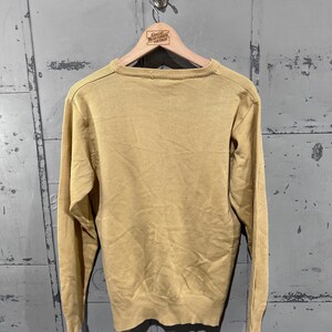 May include: A mustard yellow sweater with long sleeves, hanging on a wooden hanger. The hanger has the text "Great Northern Vintage" printed on it. The sweater is made of a knit material.