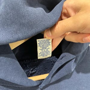 May include: A navy blue hoodie with a tag visible. The tag reads "50% Cotton (Coton) 50% Polyester Machine wash warm with like colors. Only non-chlorine bleach when needed. Tumble dry low."