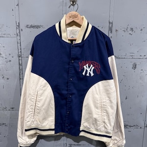 Può includere: Giacca da baseball vintage dei Yankees blu navy e color crema. La giacca presenta il logo e la scritta della squadra in rosso e bianco. Ha una chiusura con bottoni, polsini a coste e un colletto.