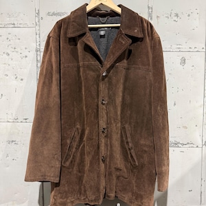 May include: A brown suede jacket with a button-up front, notched lapels, and two front pockets. The jacket is hanging on a wooden hanger against a neutral background. The jacket has a classic, timeless design.
