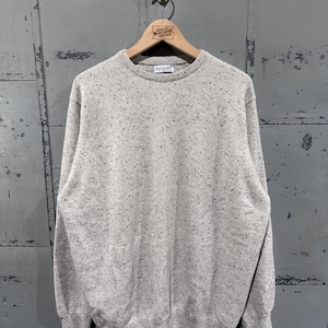 May include: A light gray crew neck sweater with a speckled pattern. The sweater has long sleeves and ribbed cuffs and hem. The brand name "epaulet" is visible on the neckline. The sweater is hanging on a wooden hanger.