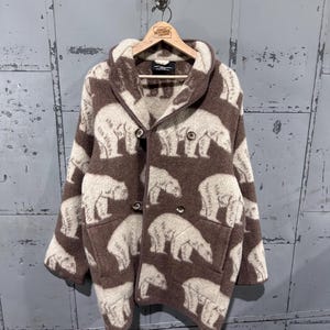May include: Brown and cream-colored fleece jacket featuring a repeating pattern of polar bears. The jacket has a double-breasted closure with two rows of buttons, a notched collar, and two front pockets. The jacket is hanging on a wooden hanger.