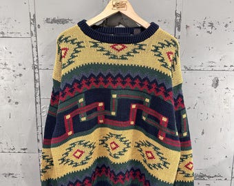 May include: A long-sleeve knit sweater featuring a multi-colored geometric pattern in shades of mustard yellow, navy blue, forest green, and deep red. The garment has a ribbed crew neckline, ribbed cuffs, and a ribbed hem in solid navy blue.