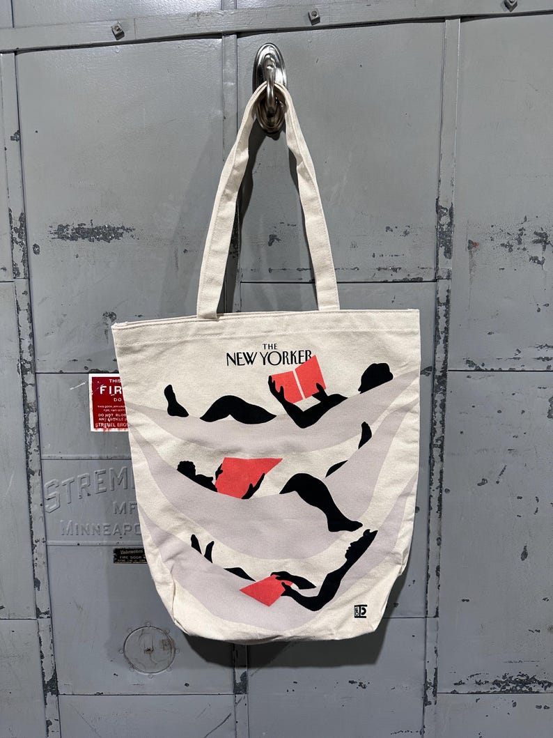 May include: Cream-colored tote bag featuring the text "THE NEW YORKER" above an illustration of figures reading books. The illustration has black figures with red books and light gray wavy lines. The bag has two cream-colored handles.