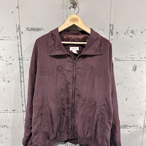 May include: A plum-colored jacket with a full zipper closure, a stand-up collar, and a ribbed hem. The jacket is hanging on a wooden hanger. The brand name "DOOARS" is visible on the label. The jacket is made of a lightweight, possibly silky material.