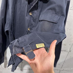May include: Navy blue jacket with a button-up front, a small chest pocket, and a collar. The jacket has a zipper closure at the neck and a buckle detail on the sleeve. The label reads "Abercrombie".