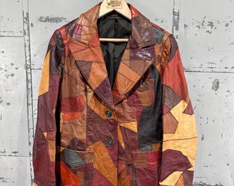 May include: A patchwork leather blazer featuring a multi-colored design with shades of brown, tan, red, and burgundy. The jacket has a notched lapel, two front buttons, and three patch pockets with flaps. It is lined with black fabric.