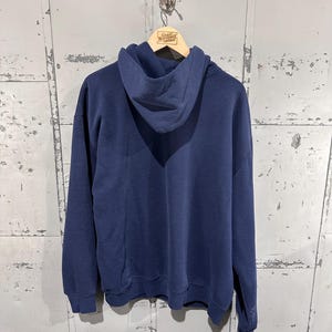May include: A navy blue hoodie with a drawstring hood and long sleeves. The hoodie is hanging on a wooden hanger. The tag on the hanger reads "Great Northern Vintage".