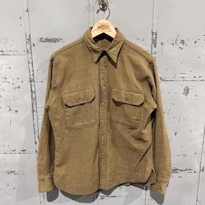 May include: A long-sleeved, button-down shirt in a muted olive green color. The shirt features two chest pockets and a classic collar. The shirt is hanging on a wooden hanger with the text "GREAT NORTHERN VINTAGE".