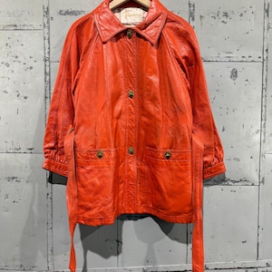 May include: A vintage orange leather jacket with a collared neckline, long sleeves, and a matching belt. The jacket features gold-colored buttons and two front pockets. The label reads "Theodore's".