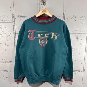May include: Teal-colored sweatshirt with the word "Tech" in a vintage font across the chest. The sweatshirt has maroon and tan accents on the collar and cuffs. A crest graphic is below the word "Tech".