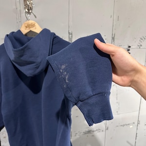 May include: Navy blue hoodie with a drawstring hood and ribbed cuffs. The sleeve shows discoloration and a small tear. The hoodie is hanging on a wooden hanger.