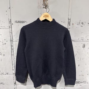Könnte beinhalten: Ein marineblauer Rollkragenpullover mit langen Ärmeln. Der Pullover ist aus Strickstoff gefertigt und hängt an einem Holzkleiderbügel. Der Kleiderbügel hat ein kleines Etikett mit der Aufschrift "Great Northwest Vintage".