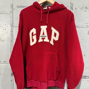 May include: Red fleece hoodie with a white "GAP Athletic" logo on the front.