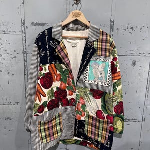 May include: A patchwork blazer with a variety of patterns, including gingham, plaid, and floral prints. The blazer features a collage of vegetables and the text "Howning's Tavern" on a patch. The jacket is hanging on a wooden hanger.