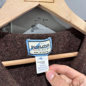 K&ouml;nnte beinhalten: Ein brauner Wollpullover mit einem Pendleton Originals Etikett mit dem Text Pendleton Originals Born in Oregon. Ein wei&szlig;es Zusatzetikett zeigt die Gr&ouml;&szlig;e XL, RN 29685, 100% Wool, Made in Hong Kong und den Hinweis See Reverse for Care.