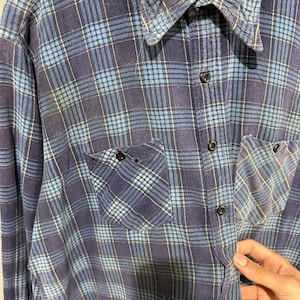 Pu&ograve; includere: Una camicia a maniche lunghe con bottoni caratterizzata da un motivo a quadri blu e blu navy con sottili linee gialle. La camicia presenta un colletto a punta, due tasche sul petto con bottoni e un'etichetta sul collo con la scritta FLANNELCRAFT 100% COTTON.