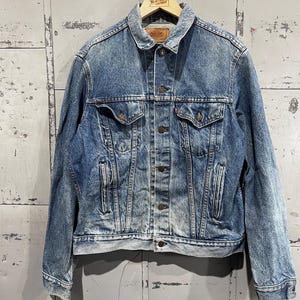 May include: A vintage blue denim jacket with a button closure, two chest pockets, and two front pockets. The jacket has a faded look and is in good condition.