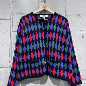 May include: A black cardigan with a diamond pattern in red, green, and blue. The cardigan has a button closure and two pockets.