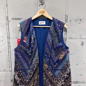 May include: A quilted vest with a patchwork design in shades of blue, purple, and floral patterns. The vest has a navy blue lining and two front pockets. The label reads "Matisse".