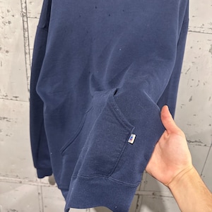 May include: Navy blue hoodie with a kangaroo pocket and a drawstring hood. The sweatshirt has a small white and red tag on the sleeve. The fabric appears to be a soft, medium-weight material.